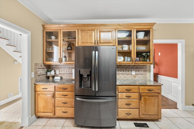 kitchen with light stone countertops, stainless steel refrigerator with ice dispenser, backsplash, ornamental molding, and light tile patterned floors