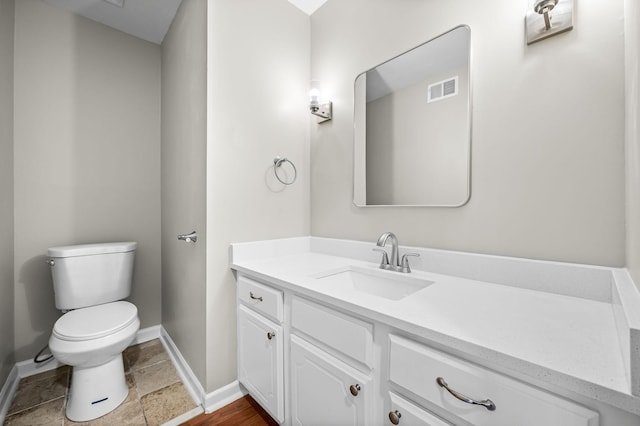 half bath with baseboards, visible vents, vanity, and toilet