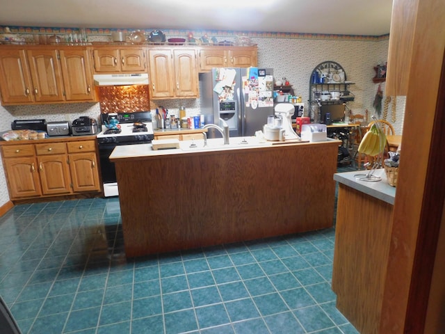 kitchen with stainless steel fridge, sink, dark tile patterned flooring, an island with sink, and white gas stove