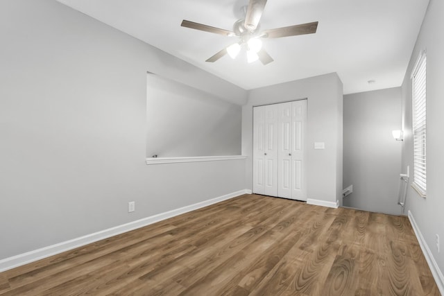 unfurnished bedroom featuring ceiling fan, a closet, hardwood / wood-style floors, and multiple windows