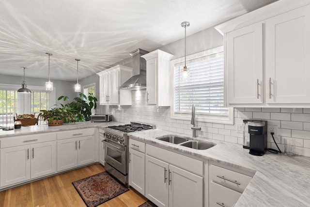 kitchen featuring high end range, pendant lighting, sink, white cabinets, and wall chimney exhaust hood