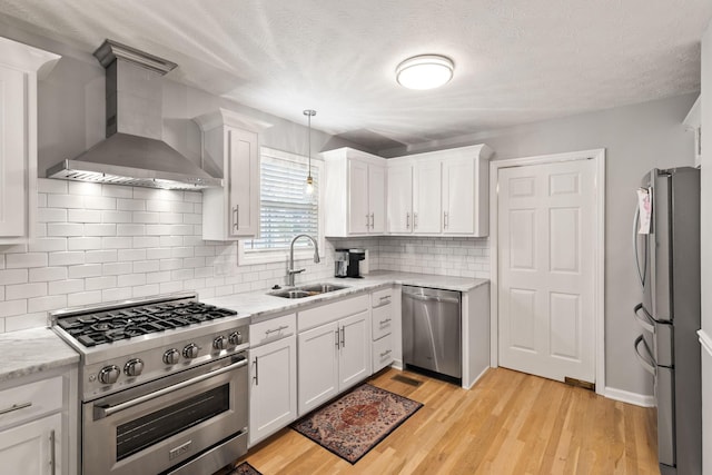 kitchen featuring sink, wall chimney range hood, appliances with stainless steel finishes, and white cabinets