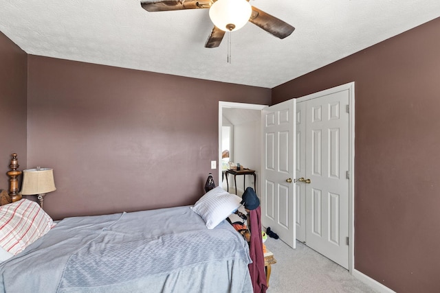 bedroom with light carpet, ceiling fan, a textured ceiling, and a closet