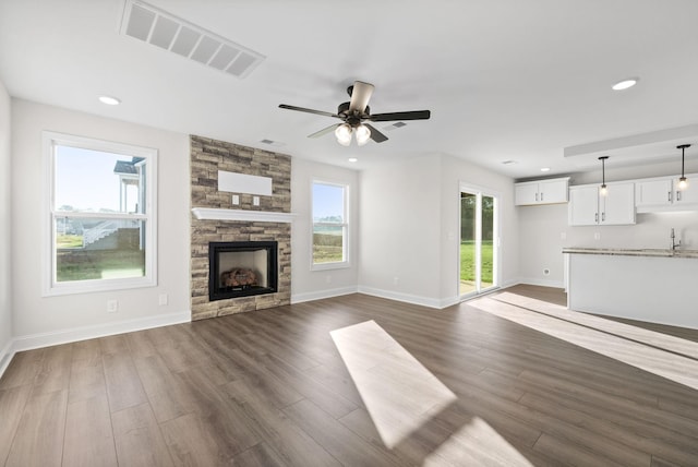 unfurnished living room featuring ceiling fan, dark hardwood / wood-style floors, a stone fireplace, and sink