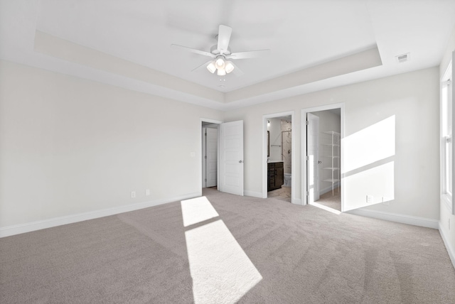 unfurnished bedroom featuring ensuite bathroom, ceiling fan, and a raised ceiling