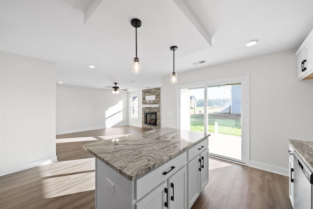 kitchen with ceiling fan, a kitchen island, white cabinetry, hanging light fixtures, and light stone counters