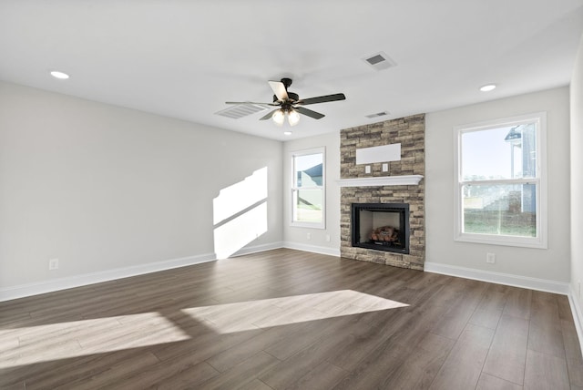 unfurnished living room featuring ceiling fan, a healthy amount of sunlight, dark wood-type flooring, and a stone fireplace