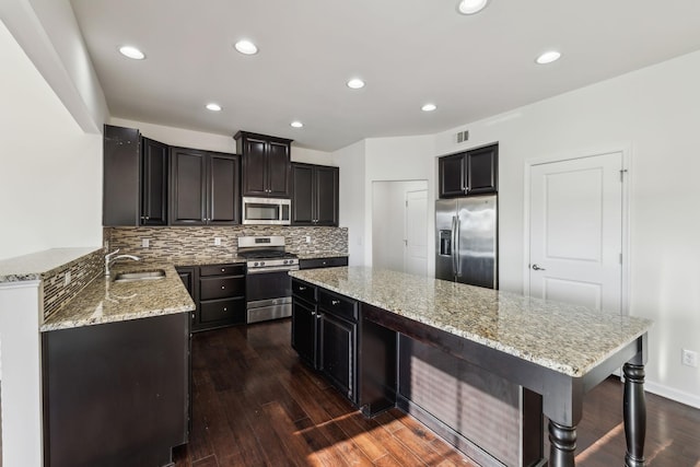 kitchen featuring appliances with stainless steel finishes, dark hardwood / wood-style floors, tasteful backsplash, light stone countertops, and sink