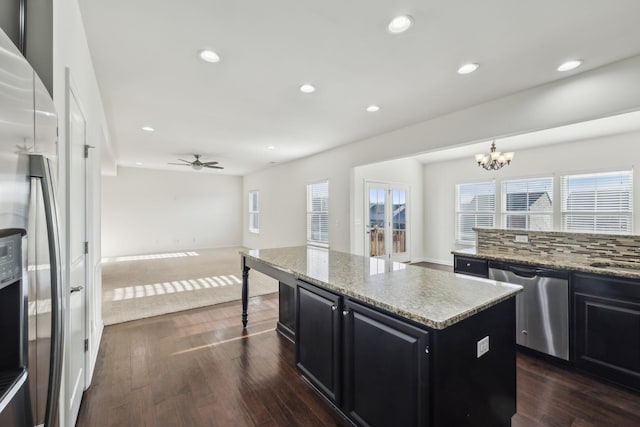 kitchen featuring ceiling fan with notable chandelier, appliances with stainless steel finishes, a center island, decorative light fixtures, and backsplash