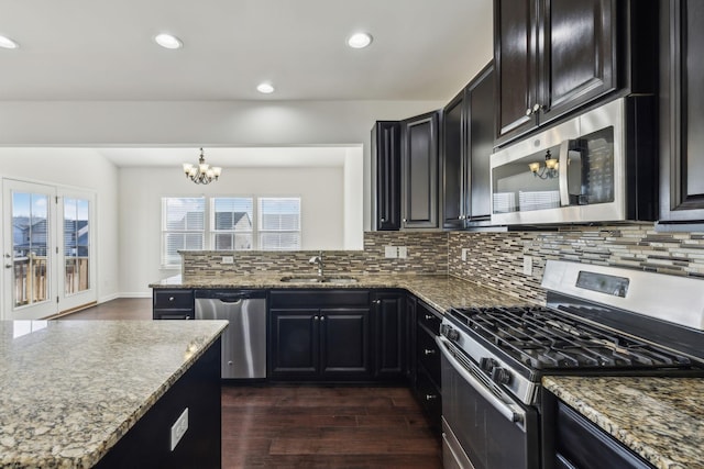 kitchen with stainless steel appliances, decorative light fixtures, stone counters, a chandelier, and sink