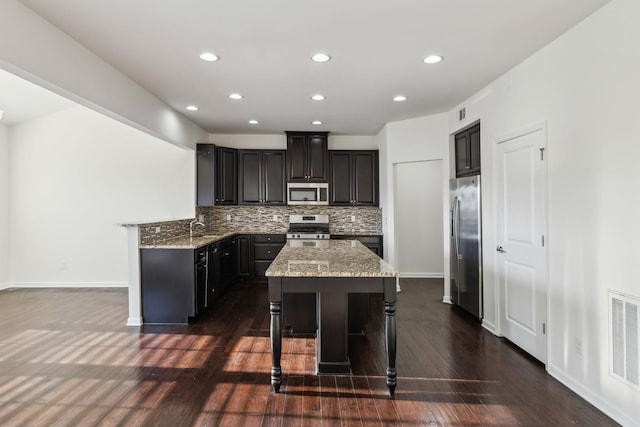 kitchen with stainless steel appliances, decorative backsplash, dark hardwood / wood-style floors, and a breakfast bar