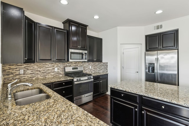 kitchen with dark hardwood / wood-style floors, decorative backsplash, sink, light stone countertops, and appliances with stainless steel finishes