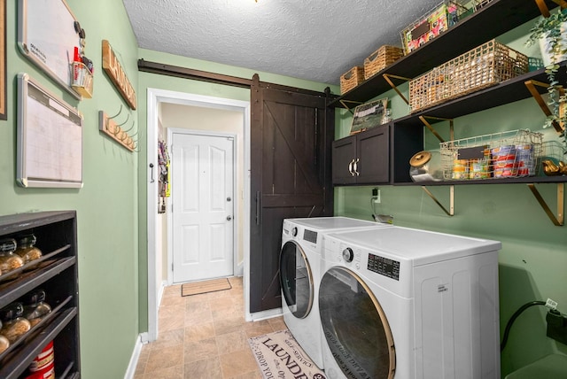 washroom with a barn door, washer and dryer, a textured ceiling, and cabinets