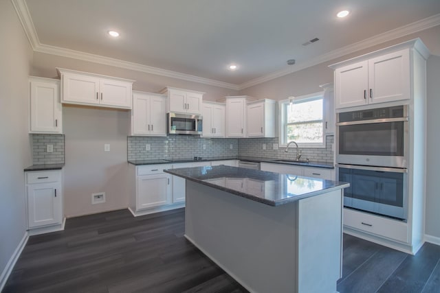 kitchen with appliances with stainless steel finishes, white cabinets, a kitchen island, and sink