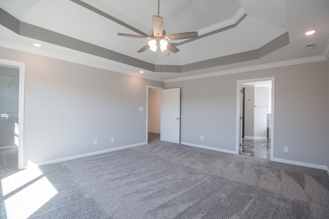 unfurnished bedroom with ceiling fan, crown molding, a tray ceiling, carpet flooring, and a walk in closet