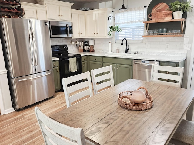 kitchen featuring light hardwood / wood-style floors, appliances with stainless steel finishes, decorative light fixtures, green cabinetry, and sink