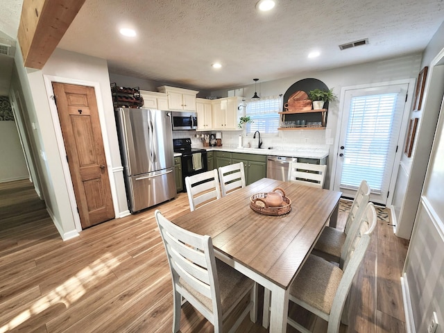 kitchen featuring appliances with stainless steel finishes, decorative light fixtures, light hardwood / wood-style floors, backsplash, and green cabinetry