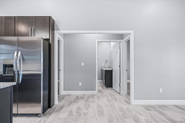 kitchen featuring light stone countertops, stainless steel refrigerator with ice dispenser, sink, light wood-type flooring, and dark brown cabinets