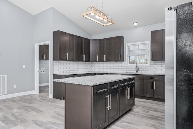 kitchen with a barn door, vaulted ceiling, a kitchen island, stainless steel refrigerator, and light hardwood / wood-style flooring