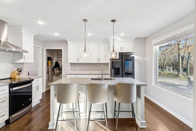 kitchen featuring decorative light fixtures, a center island with sink, stainless steel appliances, and wall chimney exhaust hood