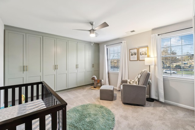 bedroom with ceiling fan, light carpet, a closet, and a crib