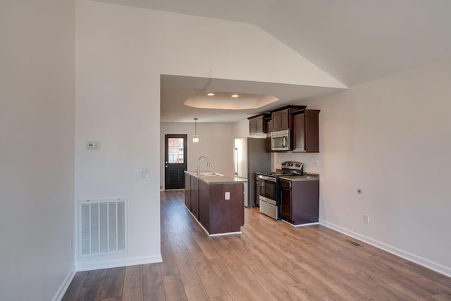 kitchen featuring sink, appliances with stainless steel finishes, dark brown cabinets, an island with sink, and light wood-type flooring