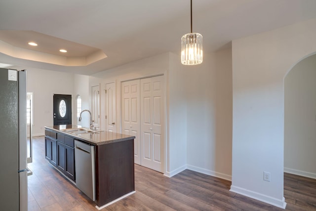 kitchen with decorative light fixtures, sink, stainless steel appliances, dark wood-type flooring, and a center island with sink