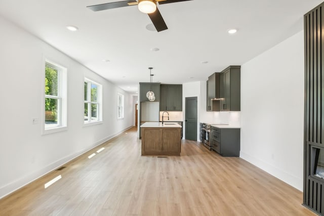 kitchen with ceiling fan, high end range, a center island with sink, sink, and light wood-type flooring