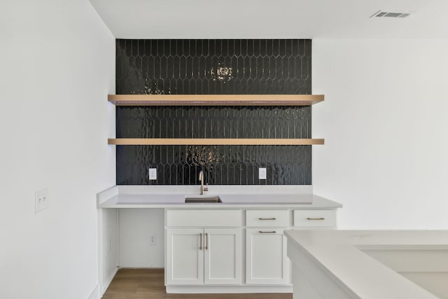 bar featuring light hardwood / wood-style flooring, white cabinets, backsplash, and sink