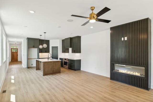 kitchen with pendant lighting, light hardwood / wood-style floors, electric stove, sink, and a kitchen island with sink