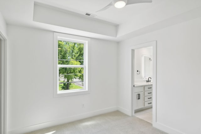 spare room featuring ceiling fan, light colored carpet, and a raised ceiling