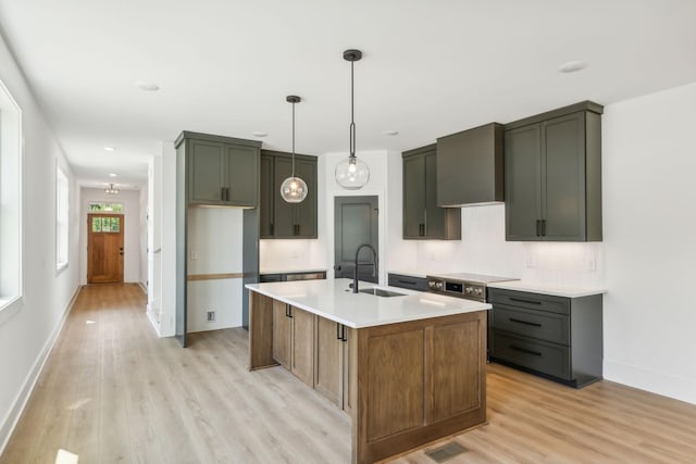 kitchen featuring pendant lighting, wall chimney exhaust hood, an island with sink, light hardwood / wood-style floors, and sink