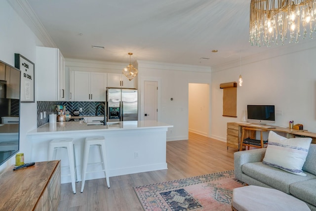 kitchen with pendant lighting, white cabinets, stainless steel fridge, kitchen peninsula, and light hardwood / wood-style flooring