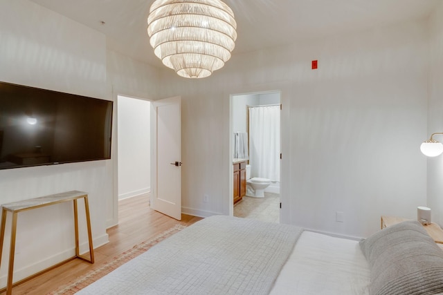 bedroom with light wood-type flooring, a chandelier, and connected bathroom