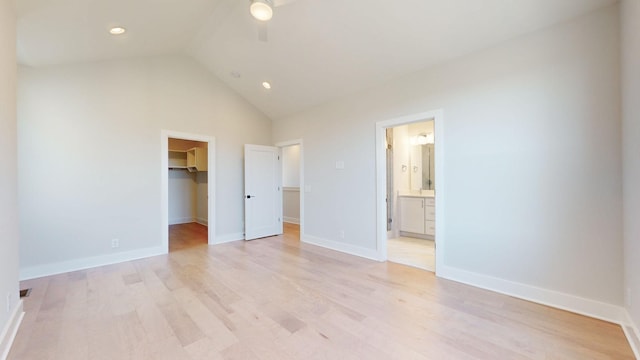 unfurnished bedroom featuring ensuite bathroom, a spacious closet, vaulted ceiling, light hardwood / wood-style flooring, and a closet