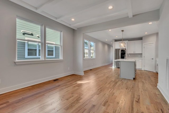 kitchen featuring decorative light fixtures, white cabinetry, beamed ceiling, stainless steel refrigerator, and a center island with sink