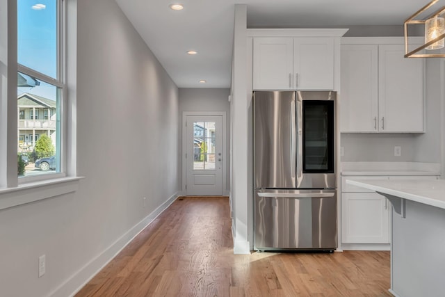 kitchen with white cabinets, pendant lighting, stainless steel fridge, and light hardwood / wood-style flooring