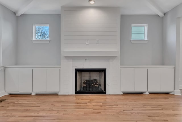 unfurnished living room featuring lofted ceiling with beams, plenty of natural light, a premium fireplace, and light hardwood / wood-style flooring