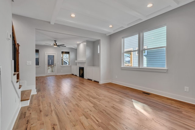 unfurnished living room featuring ceiling fan, light wood-type flooring, beamed ceiling, and a fireplace