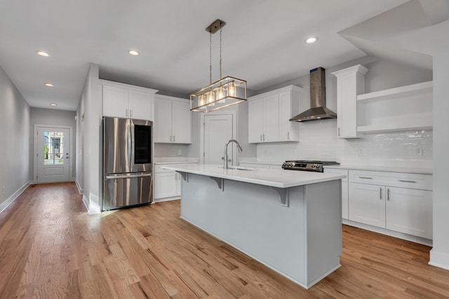 kitchen featuring white cabinetry, decorative light fixtures, wall chimney range hood, and stainless steel refrigerator