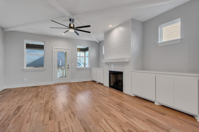 unfurnished living room featuring a wealth of natural light, a large fireplace, light hardwood / wood-style floors, and beamed ceiling