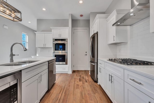 kitchen featuring stainless steel appliances, tasteful backsplash, wall chimney range hood, white cabinets, and sink