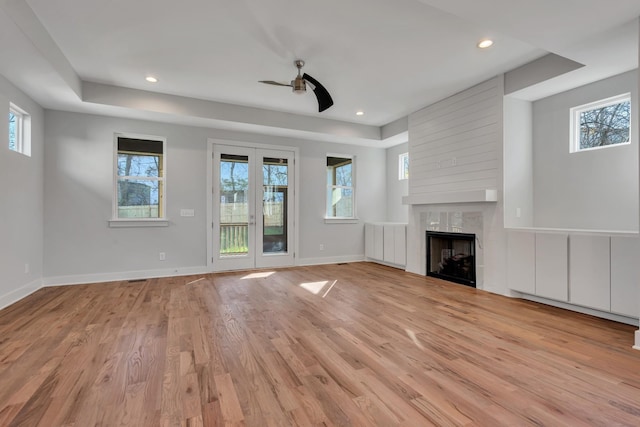 unfurnished living room featuring light wood-type flooring, ceiling fan, a high end fireplace, and french doors