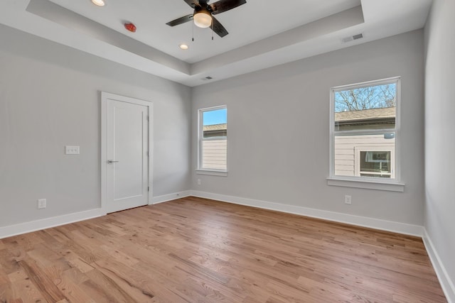 spare room with ceiling fan, light hardwood / wood-style flooring, and a tray ceiling