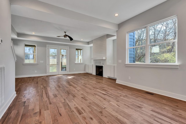 unfurnished living room featuring ceiling fan, a healthy amount of sunlight, a fireplace, and light hardwood / wood-style flooring