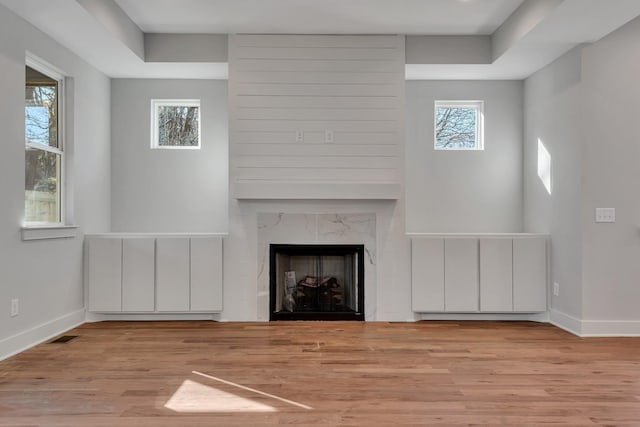 unfurnished living room featuring a high end fireplace, a wealth of natural light, and light hardwood / wood-style flooring