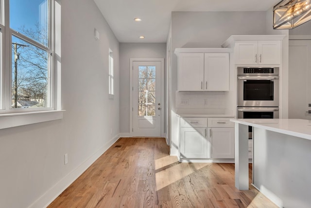 kitchen with backsplash, white cabinets, double oven, and light hardwood / wood-style flooring