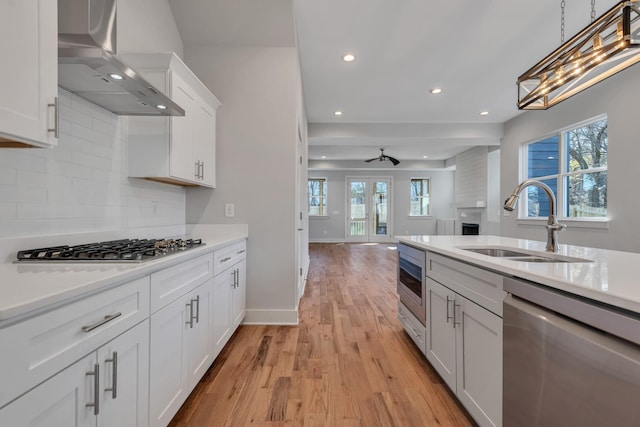 kitchen with ceiling fan, stainless steel appliances, wall chimney exhaust hood, white cabinets, and sink