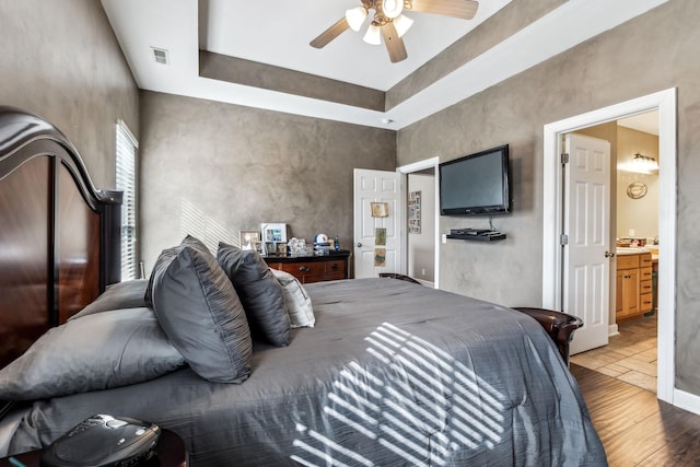 bedroom featuring ceiling fan, hardwood / wood-style flooring, a tray ceiling, and ensuite bath