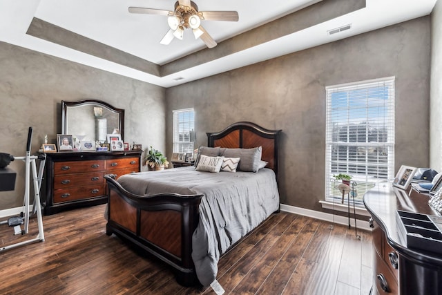 bedroom featuring ceiling fan, dark hardwood / wood-style flooring, a tray ceiling, and multiple windows